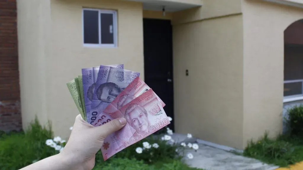 Persona sostiene dinero frente a una casa.