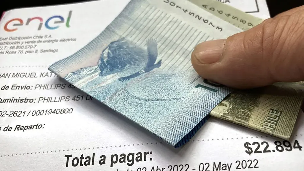 Una mano sostiene una cuenta de la luz junto con unos billetes de $10.000 y $1.000.
