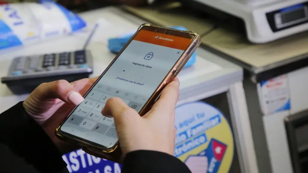 Una mujer abre la app de Banco Estado en su teléfono para pagar una compra en un almacén con el Bolsillo Familiar Electrónico.