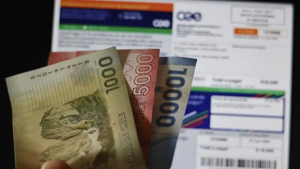 Una mano sostiene billetes frente a una boleta de la luz