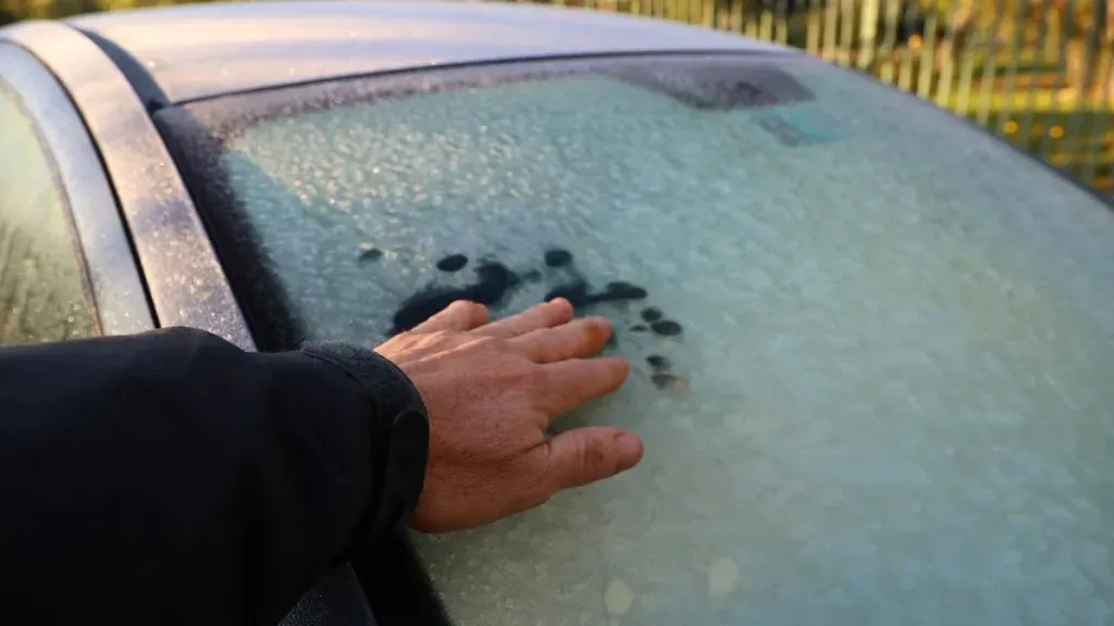 Una mano toca el parabrisas escarchado de un auto rojo.