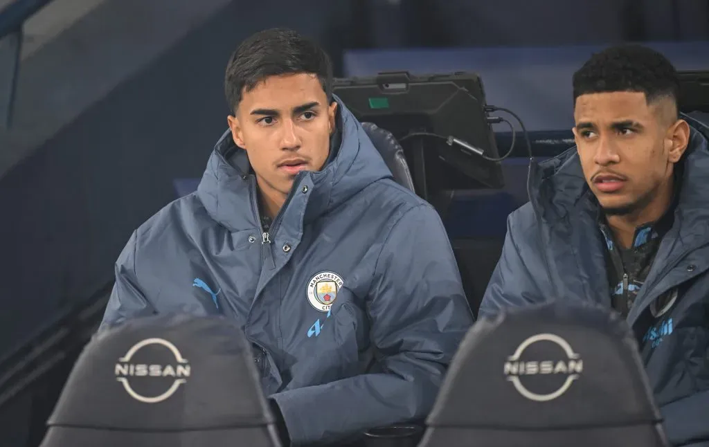 Vitor Reis, do Manchester City, sentado, de jaqueta azul
