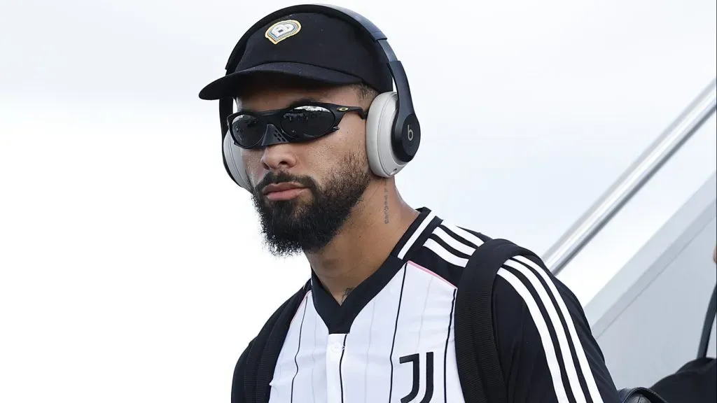 Douglas Luiz, com a camisa preta e branca listrada, com óculos preto, descendo as escadas