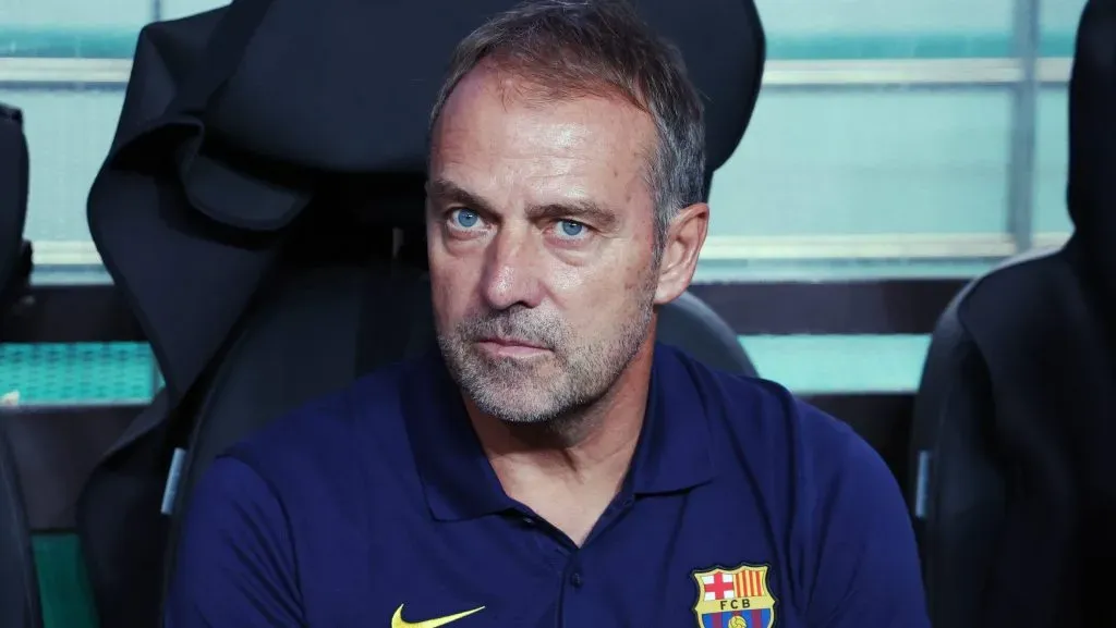 Hansi Flick, sentado, de camisa azul marinho, do Barcelona