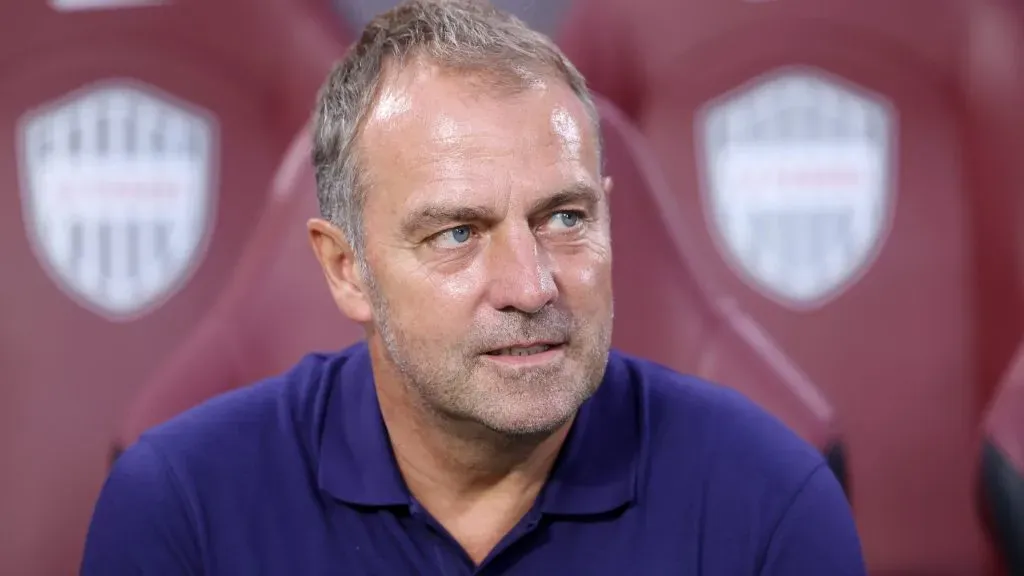 Hansi Flick, sentado, de camisa azul marinho do Barcelona