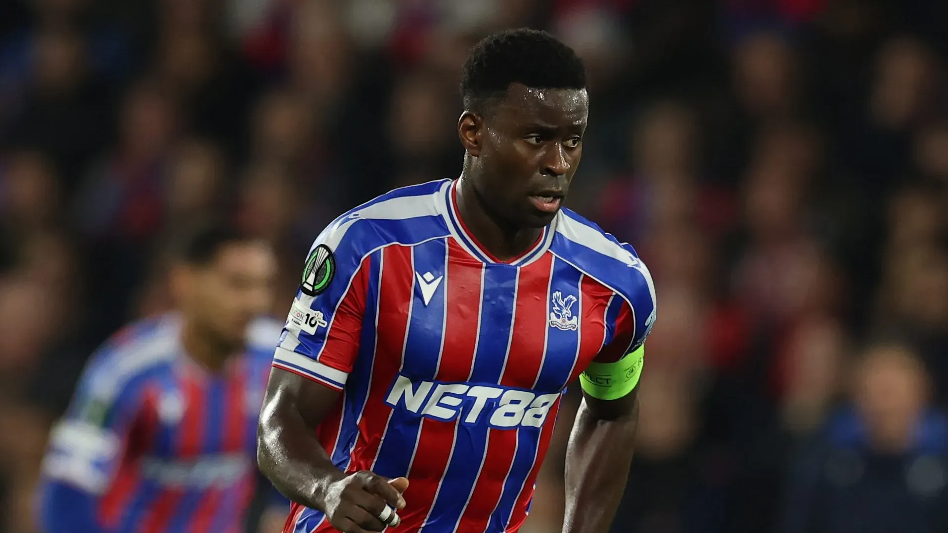 Marc Guéhi em movimento com a camisa usando a camisa azul e vermelha do Crystal Palace