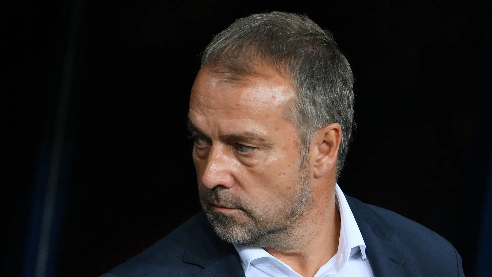 Hansi Flick, de terno, olhando para o lado em jogo do Barcelona