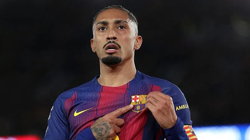 Raphinha, em campo, apontando para escudo do Barcelona