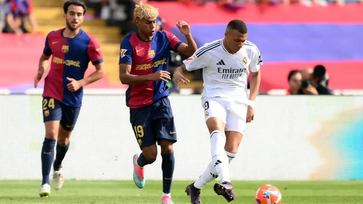 Kylian Mbappe of Real Madrid passes the ball under pressure from Lamine Yamal of FC Barcelona.
