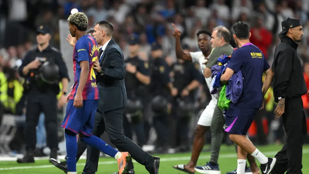 Lamine Yamal of FC Barcelona is escorted off the pitch as Vinicius Junior of Real Madrid gestures towards him.