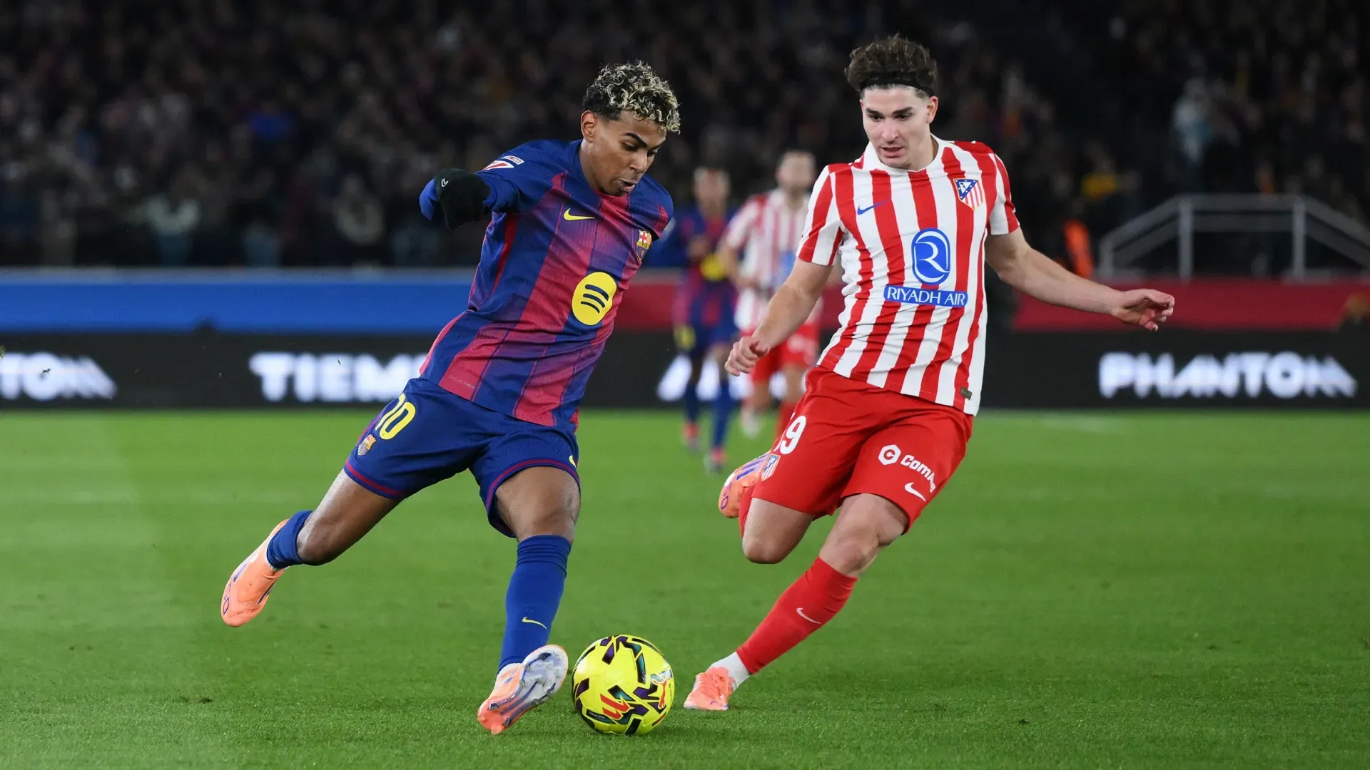 Lamine Yamal of FC Barcelona runs with the ball whilst under pressure from Julian Alvarez of Atletico de Madrid.